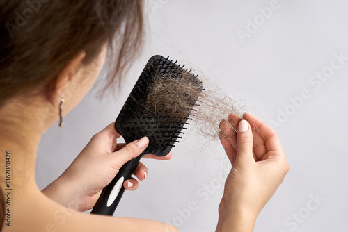 A woman is holding a hairbrush filled with a significant amount of shed hair. She is gently pulling the hair out of the brush, likely examining it.
