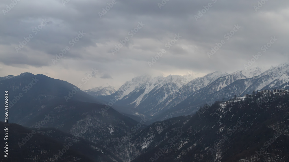 Snow-covered mountain range under grey sky, power lines visible, serene wintry landscape. Snow-covered mountain range under grey sky, power lines visible, serene wintry landscape.