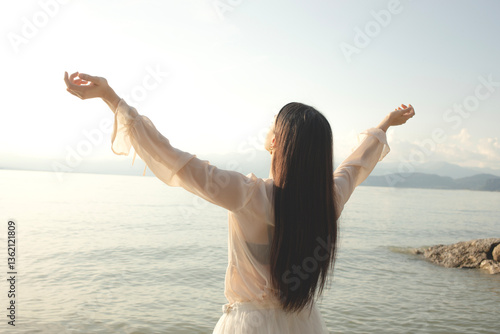 woman relaxes with her arms raised towards the sun that envelops her