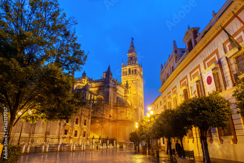 Evening view of Seville Cathedral and La Giralda tower illuminated under blue twilight sky in the historic center of Seville, Spain