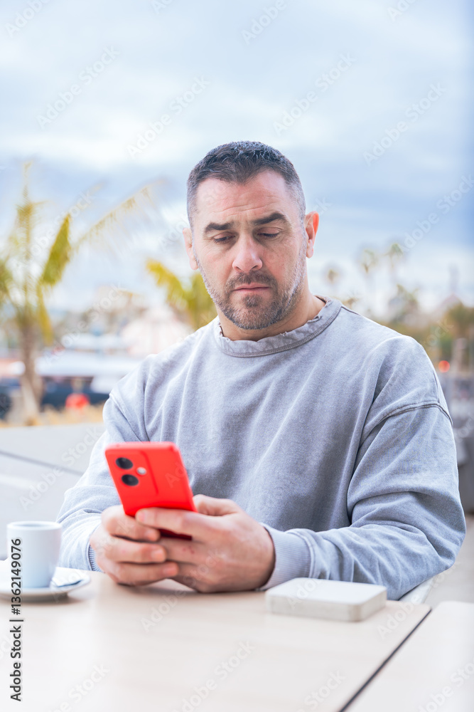 serious caucasian man, serious man looking at her mobile smart phone, typing a message on the terrace of an outdoor cafe. Addiction to social networks. App, device technology concept.Vertical serious caucasian man, serious man looking at her mobile smart phone, typing a message on the terrace of an outdoor cafe. Addiction to social networks. App, device technology concept.Vertical