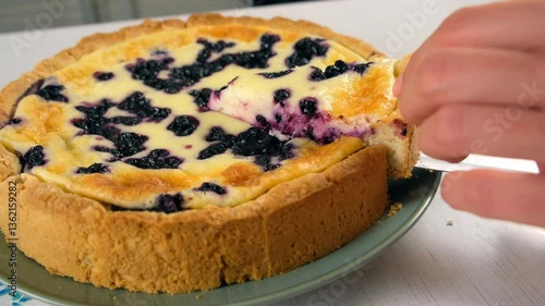 Close-up cutting piece of just baked creamy tart pie with blueberries using knife, hands close-up. Ingredient recipe cuisine culinary. Homemade meal bakery. Making preparing sweet dessert pastry.