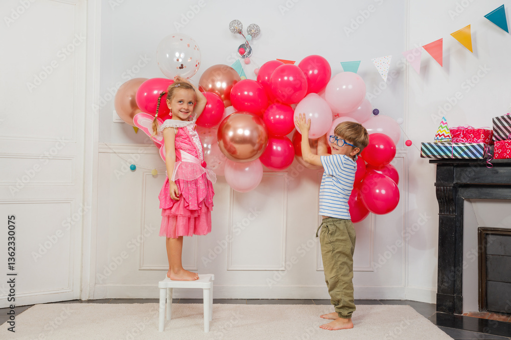 Happy kids, boy and girl hang pink balloons for fun bday party
