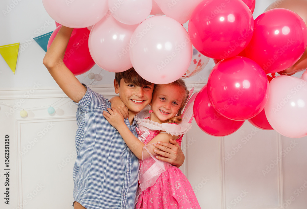 Happy brother and sister with balloons hugging at birthday party
