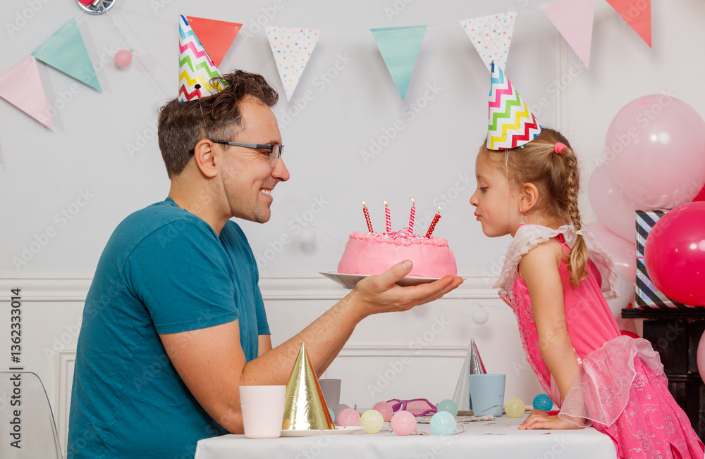 Dad holds a cake as happy daughter blows out birthday candles