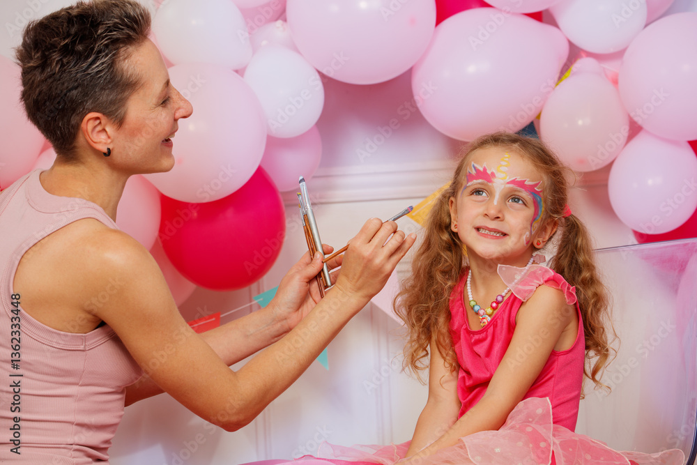 Girl sit happily as face painter apply colorful makeup at party