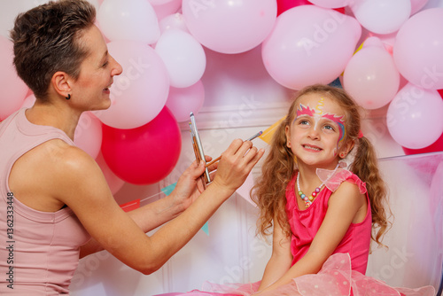 Obraz na płótnie Girl sit happily as face painter apply colorful makeup at party w salonie