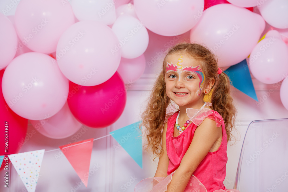 With her face being painted, the girl grins, balloons around
