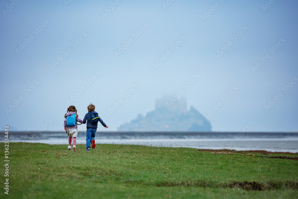 Two kids walk towards a misty Mont Saint Michel across field