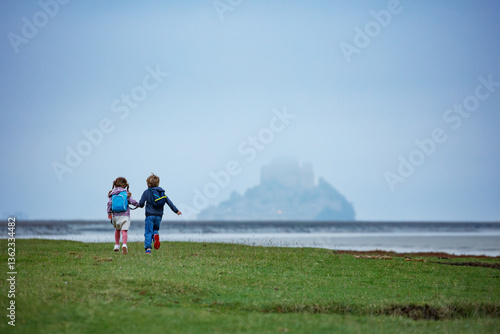 Obraz na płótnie Two kids walk towards a misty Mont Saint Michel across field w salonie