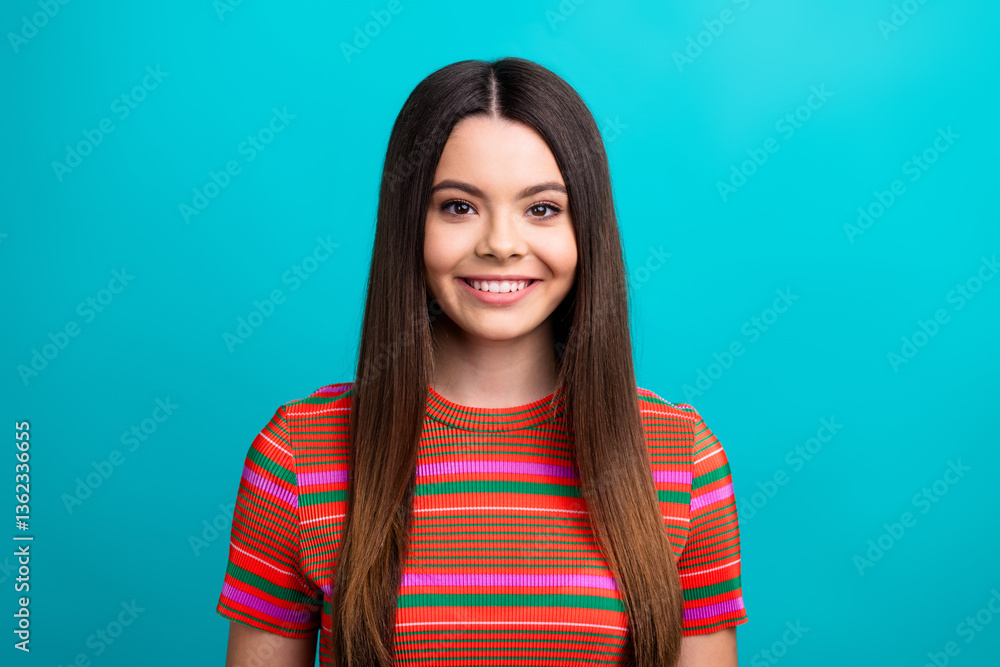 Fototapeta premium Portrait of a young woman in a colorful striped shirt smiling against a vibrant teal background, showcasing happiness and modern style