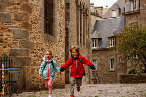 Obraz na płótnie Kids with backpacks joyfully run on a historic cobblestone path w salonie