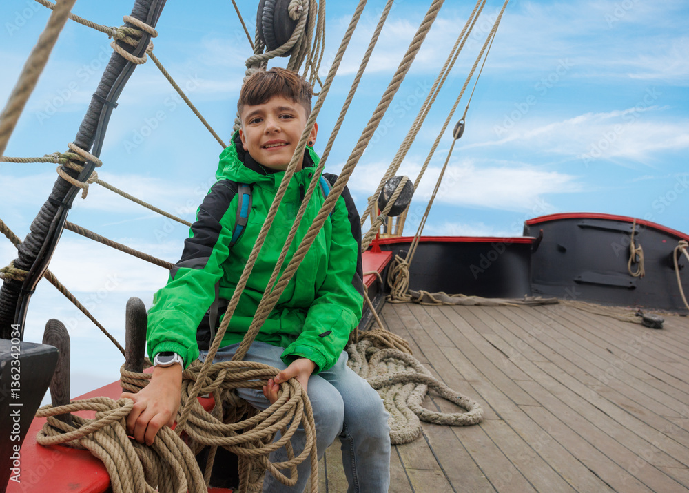 Smiling kid tourist in green explores a old pirate ship deck