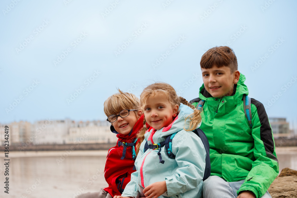 Three kids smile at beach with Saint-Malo town behind, France