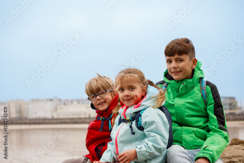 Obraz na płótnie Three kids smile at beach with Saint-Malo town behind, France w salonie