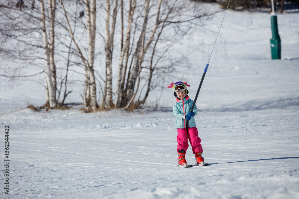 Little girl on tow lift ride at snowy slopes and funny helmet
