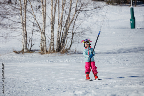 Obraz na płótnie Little girl on tow lift ride at snowy slopes and funny helmet w salonie
