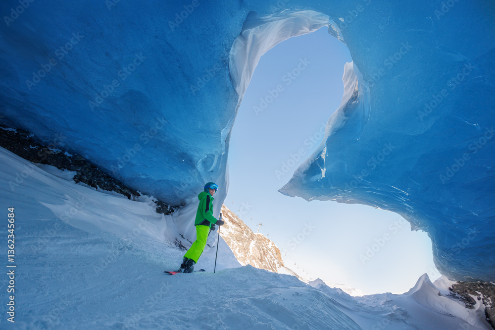 Skier boy exploring stunning ice cave with bright blue ceiling