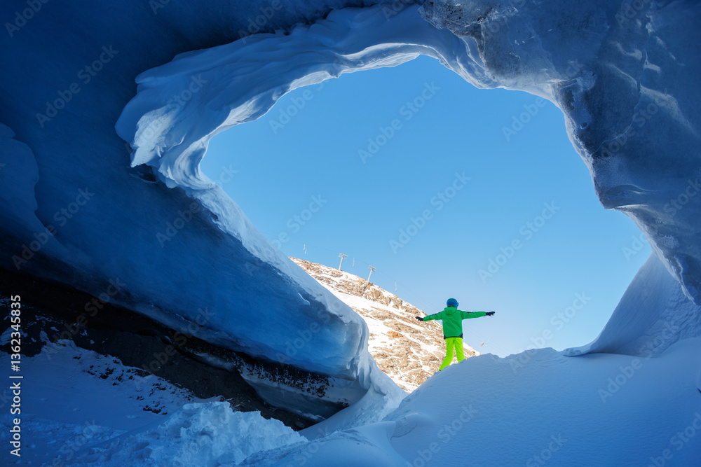 A person skier stand at the icy archway of blue glacier cavern
