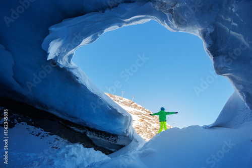 A person skier stand at the icy archway of blue glacier cavern