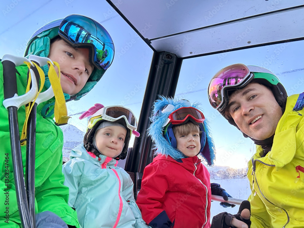 Kids with dad in colorful ski gear aboard cable car take selfie