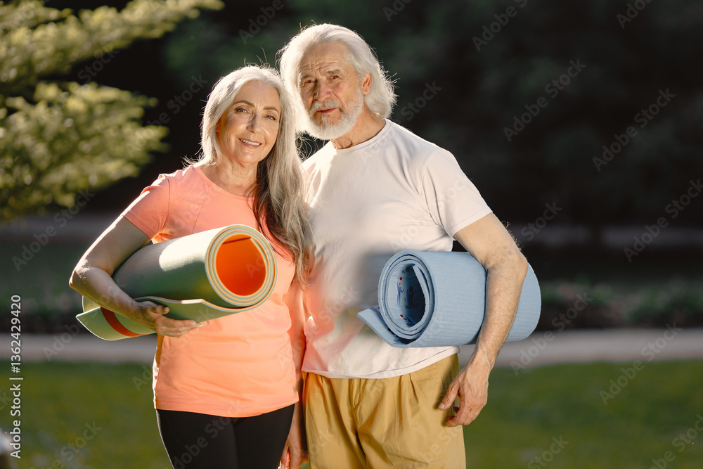 Obraz premium Senior couple with exercise mats standing at park and posing for a photo