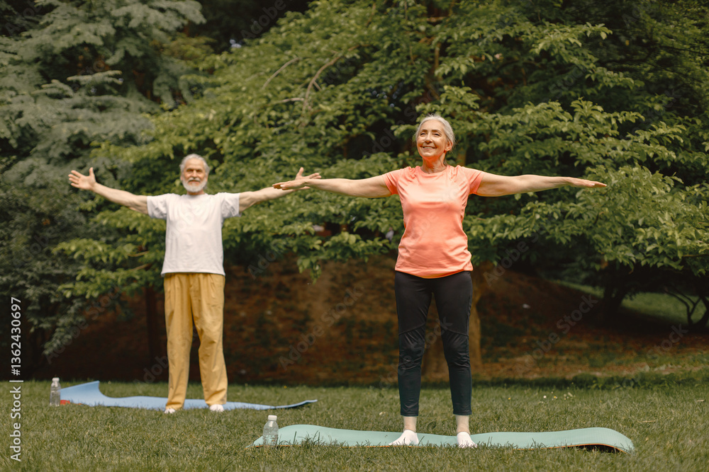 Senior couple standing at summer park and doing excercises on a yoga mats Senior couple standing at summer park and doing excercises on a yoga mats