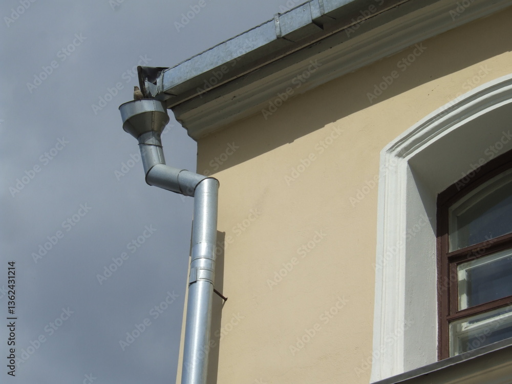 Close-up of metal rain gutter system on historic beige building under cloudy sky Close-up of metal rain gutter system on historic beige building under cloudy sky