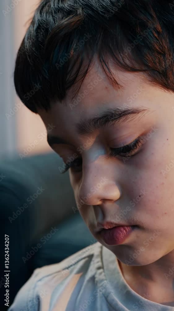 Close-up video shot of a thoughtful child, capturing a pensive expression. The angle focuses on the face, highlighting emotions and details. Live mobile wallpaper. Close-up video shot of a thoughtful child, capturing a pensive expression. The angle focuses on the face, highlighting emotions and details. Live mobile wallpaper.