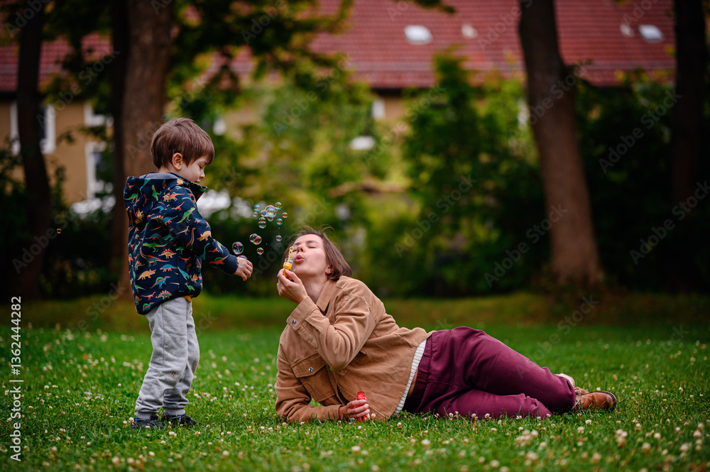 Fototapeta premium Child Playing Near Parent Blowing Bubbles in Park