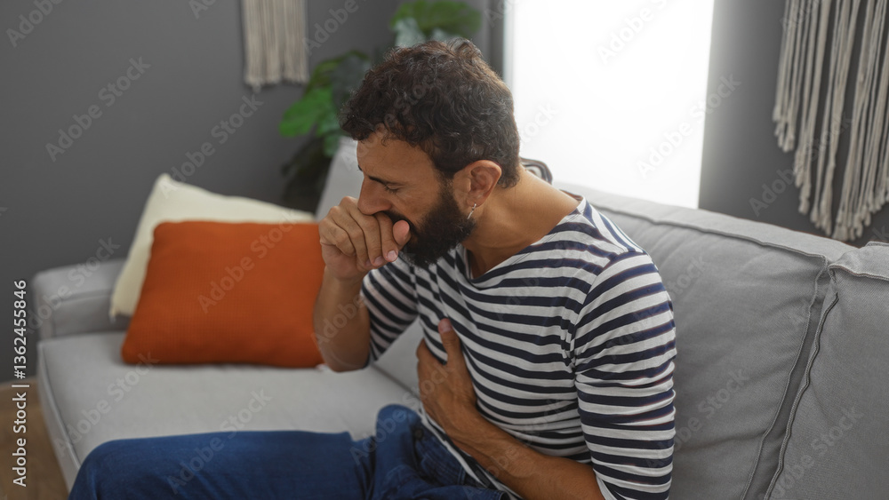 Young hispanic man with beard sitting on a sofa in a living room, coughing into his hand, wearing a striped shirt, looking unwell, with a modern home interior visible in the background. Young hispanic man with beard sitting on a sofa in a living room, coughing into his hand, wearing a striped shirt, looking unwell, with a modern home interior visible in the background.