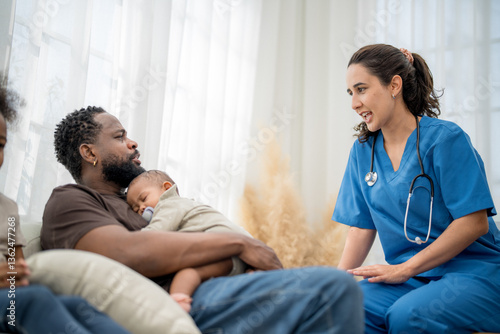 Healthcare professional talks to father holding newborn baby at home during a check-up visit
