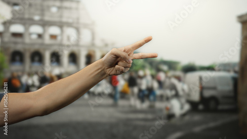 Man showing peace sign with hand in front of the iconic roman coliseum in rome, capturing the essence of outdoor city life and historical architecture.