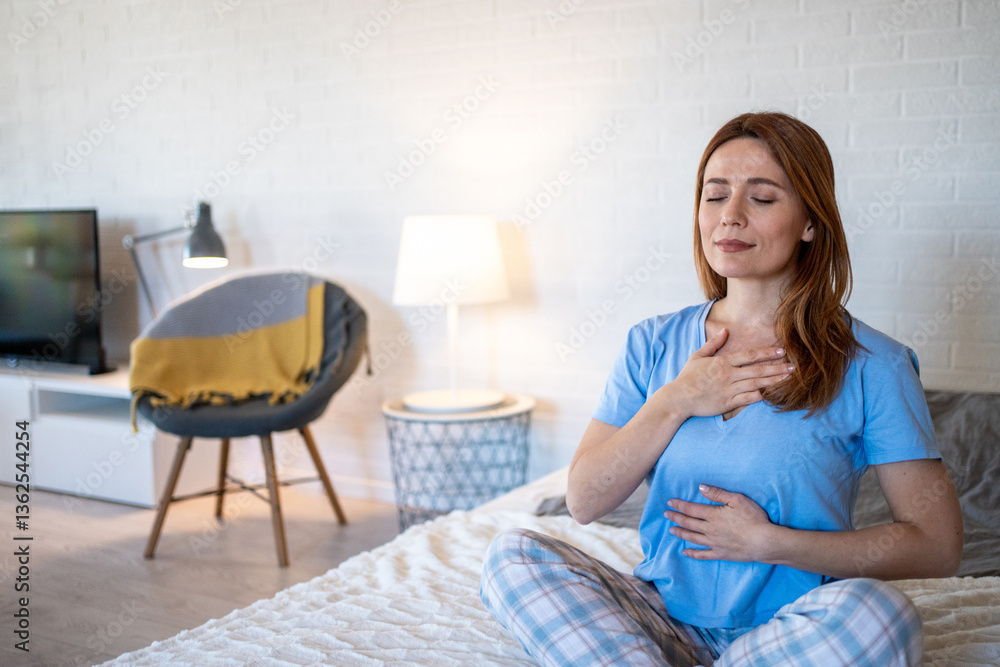 Serene woman practicing deep breathing exercise on bed in cozy bedroom Serene woman practicing deep breathing exercise on bed in cozy bedroom