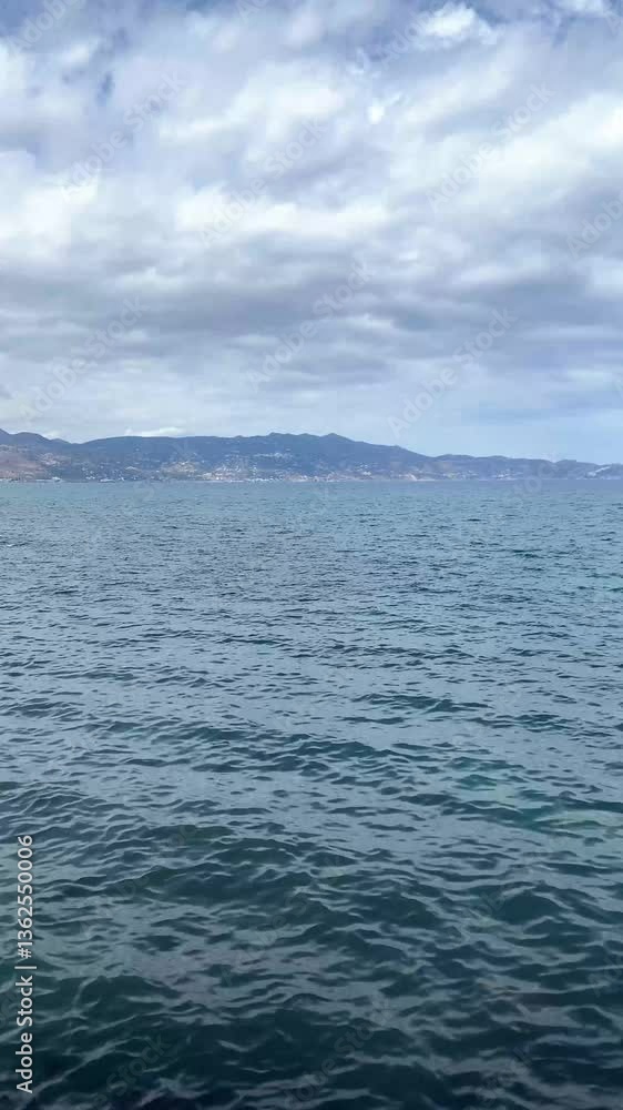 Blue calm sea around the island, mountains on the horizon, cloudy sky , vertical video Blue calm sea around the island, mountains on the horizon, cloudy sky , vertical video