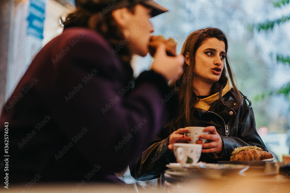 Two females sit at a cafe table, talking and enjoying hot beverages and pastries in an outdoor setting. Two females sit at a cafe table, talking and enjoying hot beverages and pastries in an outdoor setting.
