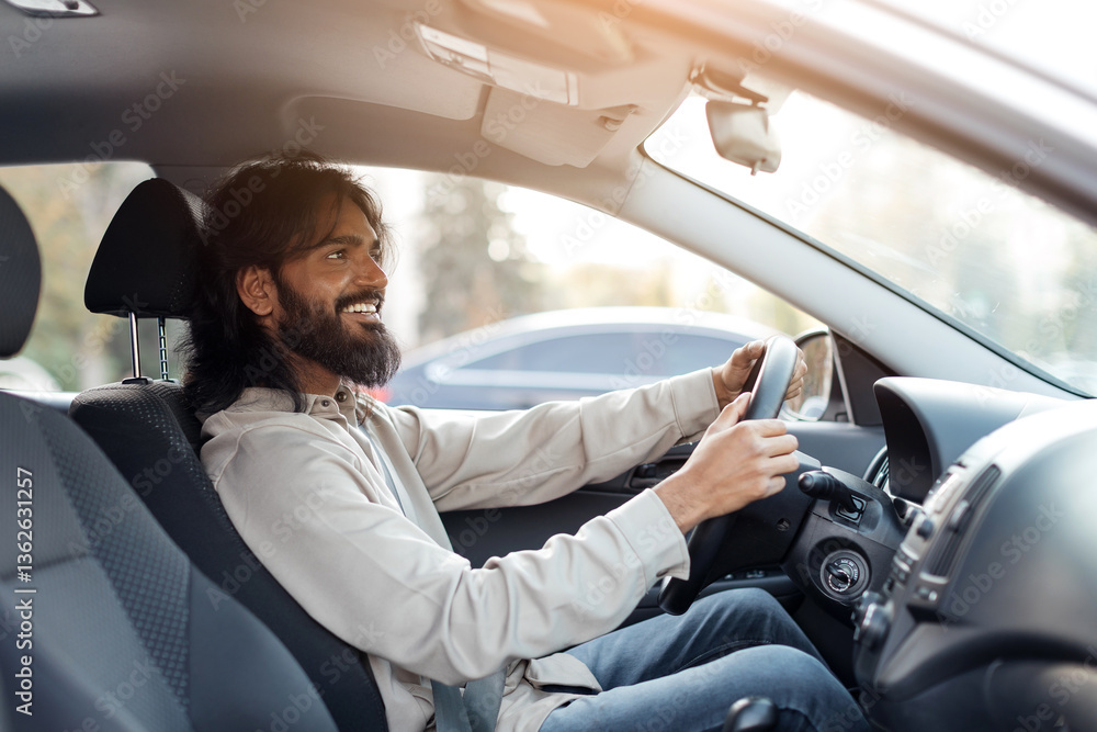 Smiling Indian man driving car and smiling, sitting in the drivers seat looking forward, relaxed eastern male enjoying the drive with both hands on the wheel, side view Smiling Indian man driving car and smiling, sitting in the drivers seat looking forward, relaxed eastern male enjoying the drive with both hands on the wheel, side view
