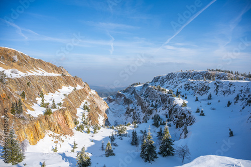 Fototapeta Naklejka Na Ścianę i Meble -  Snow blankets the Stanisław Quartz Mine at Izerskie Garby in the Izera Mountains. Pine trees dot the snowy landscape under a clear blue sky, showcasing winter's beauty in Poland.