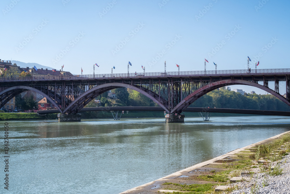 Naklejka premium Photo of the red iron arch bridge above Drava river in the center of Maribor, Slovenia.