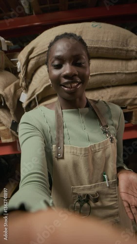 Wallpaper Mural Vertical shot of smiling, African American woman in apron talking to camera in front of shelves stocked with burlap sacks in coffee roasting plant Torontodigital.ca