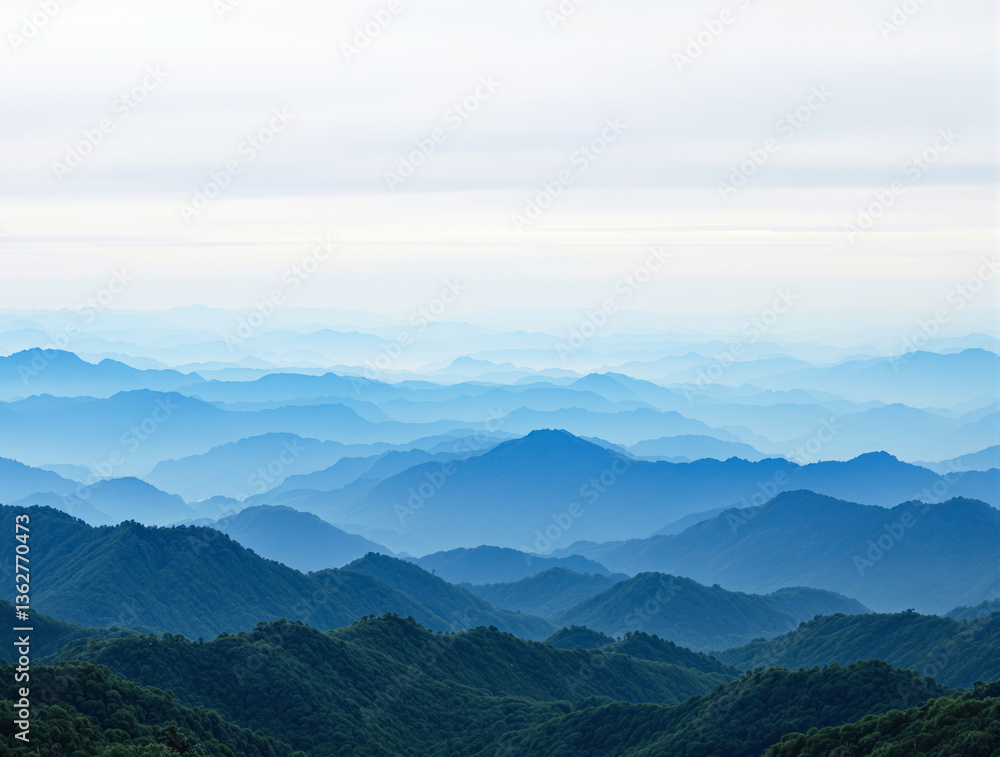 Naklejka premium Scenic mountain landscape with layers of blue ridges fading into the misty horizon under a soft, bright sky, creating a peaceful background. Ai generative
