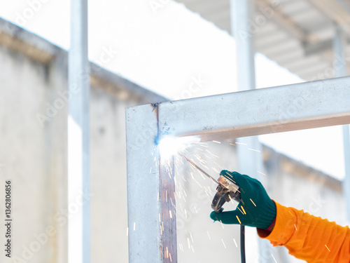 Worker welding metal bar under corner with spark.