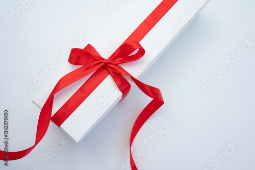 Elegant white gift box with red ribbon on white surface. International Women Week