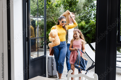 Mother and daughter arriving home with suitcase and teddy bear, smiling happily