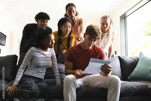 Reading acceptance college acceptance letter, diverse teenagers celebrating success on couch at home