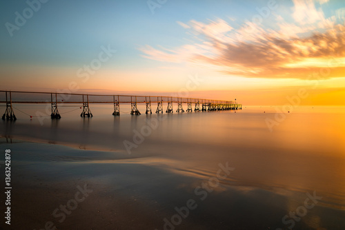 Fototapeta Naklejka Na Ścianę i Meble -  A pier in the Adriatic Sea and sunrise on the beach in Rimini, Italy. Sunrise over the sea in southern Italy. Fishing pier and rising sun