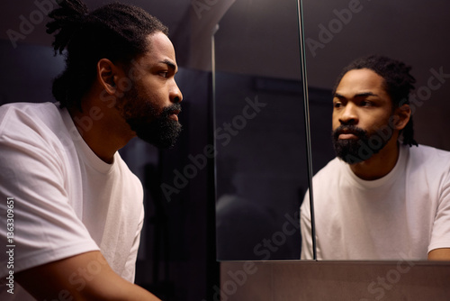 Black man looking himself in mirror in bathroom.
