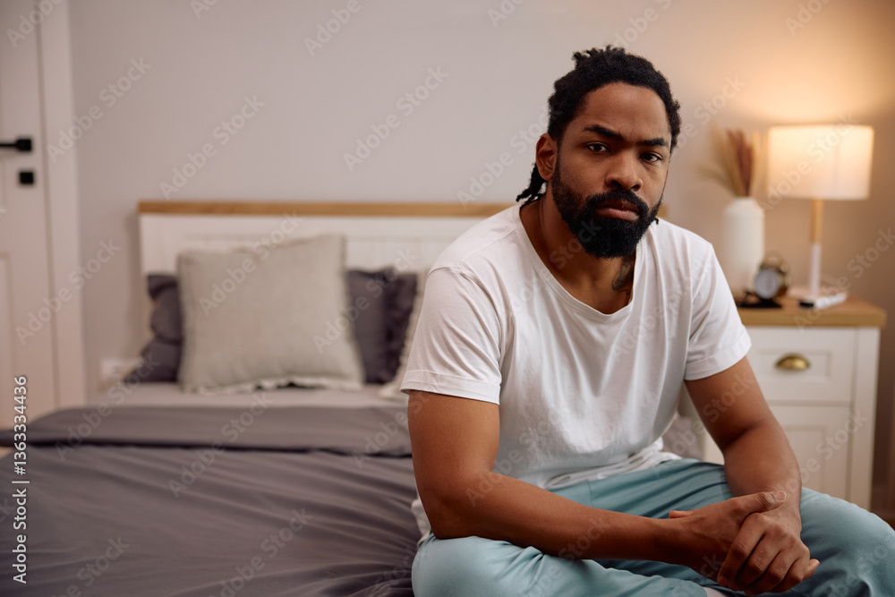 Distraught black man sitting on bed and looking at camera. Distraught black man sitting on bed and looking at camera.