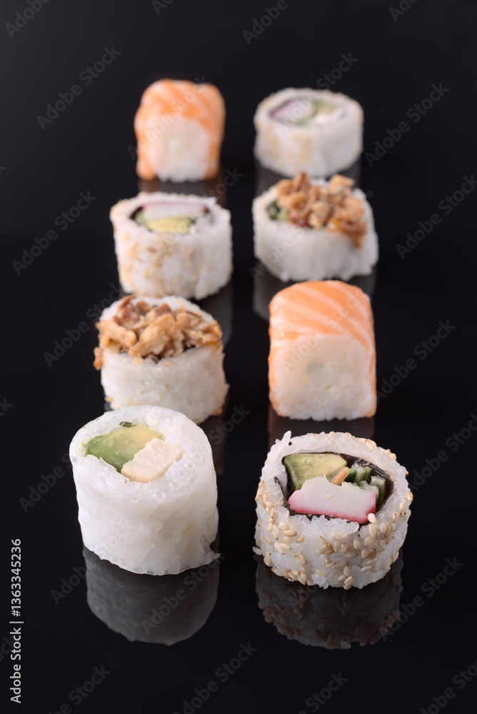 Variety of delicious sushi rolls displayed on black reflective surface Variety of delicious sushi rolls displayed on black reflective surface