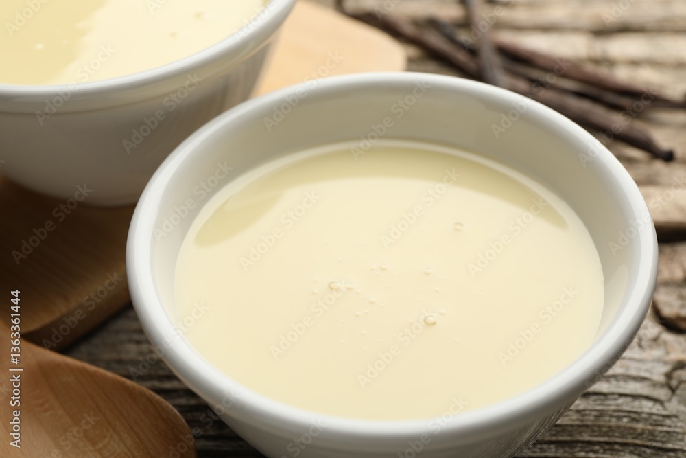 Tasty condensed milk, spoon and vanilla pods on wooden table, closeup Tasty condensed milk, spoon and vanilla pods on wooden table, closeup